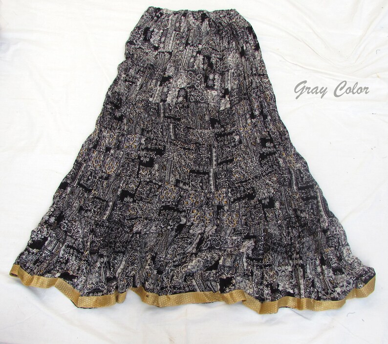 May include: A long, tiered skirt featuring a black, white, and gray patterned print with a gathered elastic waistband. The hem is finished with a solid gold-colored border. The text "Gray Color" is printed in the upper right corner of the image.