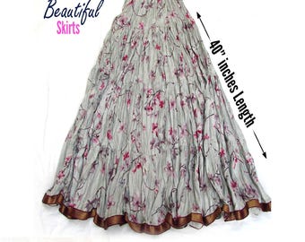 May include: A light gray tiered skirt featuring a pink and dark floral print, an elastic waistband, and a dark brown patterned border at the hem. The skirt measures 40 inches in length. Text on the image reads Beautiful Skirts and More Colors Available.