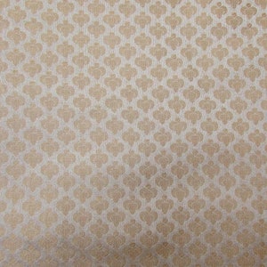 May include: A fabric featuring a repeating pattern of small, light gold spade-like shapes arranged in a grid on a textured, light beige background. The design consists of uniform, symmetrical motifs that create a consistent, dense visual texture.