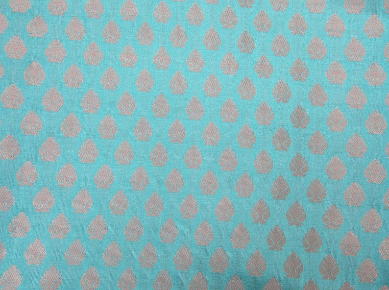 May include: A close-up of a teal fabric with a repeating pattern of light brown leaf shapes. The leaves are evenly spaced across the surface, creating a textured appearance. The fabric has a subtle sheen.
