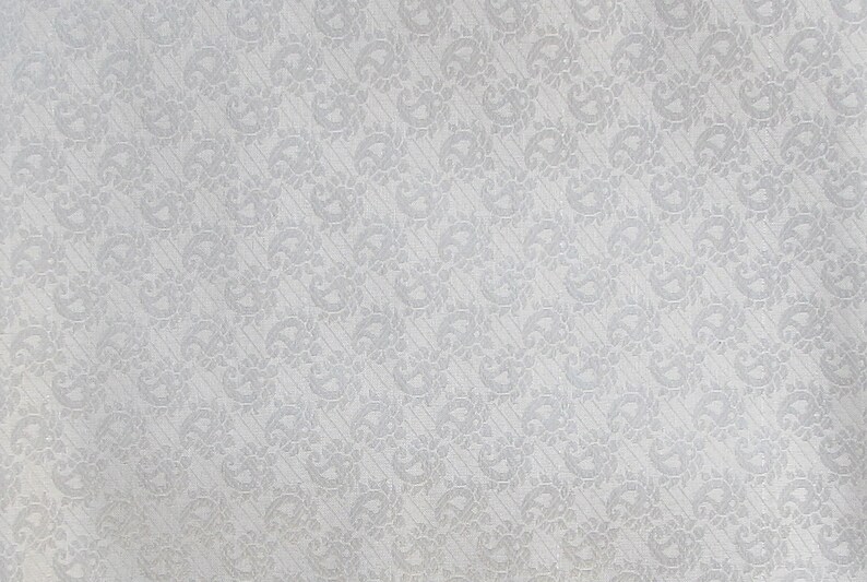 May include: A light gray fabric featuring a repeating tonal paisley pattern. The design consists of small, intricate teardrop-shaped motifs arranged in diagonal rows across the surface, creating a subtle and uniform texture throughout the material.