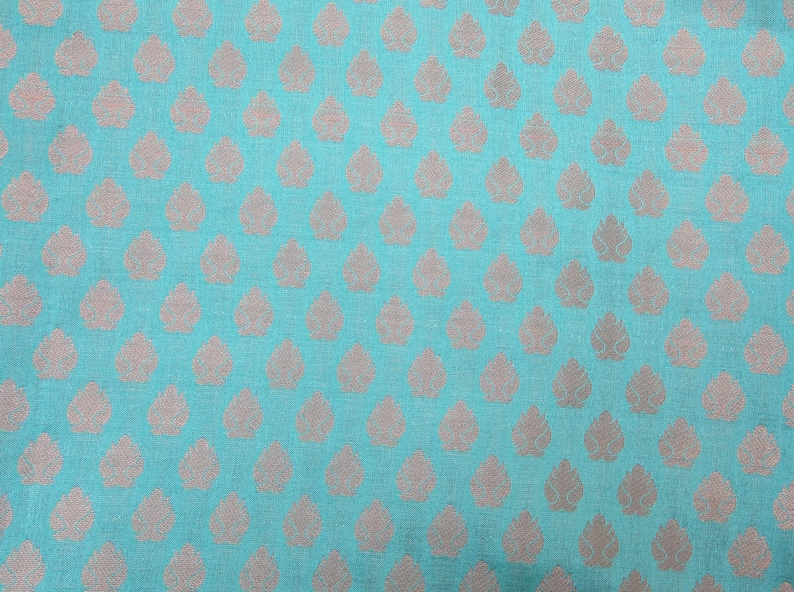 May include: A vibrant turquoise fabric featuring a repeating pattern of small, metallic silver leaf-shaped motifs arranged in a structured grid. The textile displays a visible woven texture with a consistent, uniform design across the entire surface.