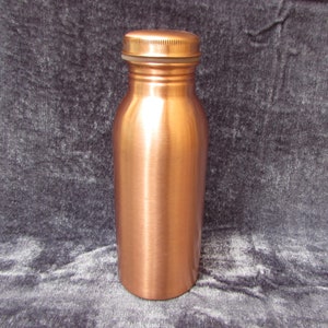 May include: A copper-colored water bottle with a screw-on lid. The bottle has a cylindrical shape with a slightly wider base and a narrow neck. The lid is the same color as the bottle. The bottle is made of metal and has a shiny finish.
