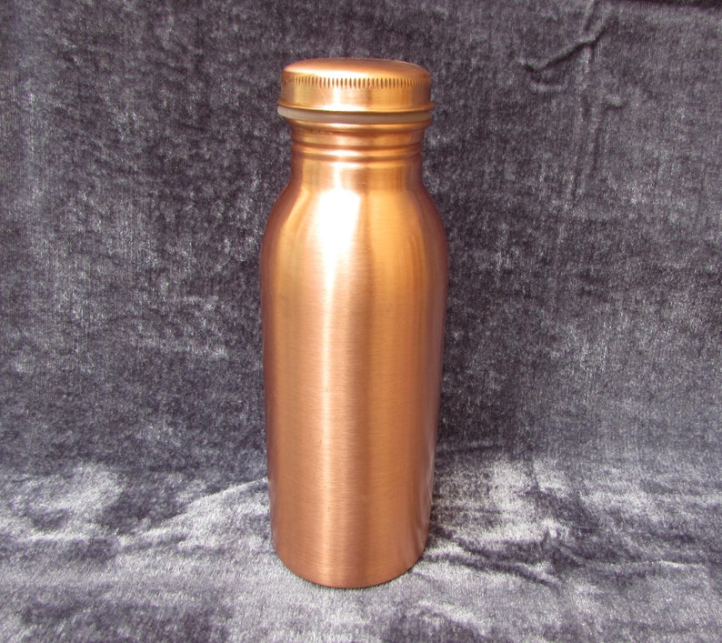 May include: A copper-colored water bottle with a screw-on lid. The bottle has a cylindrical shape with a slightly wider base and a narrow neck. The lid is the same color as the bottle. The bottle is made of metal and has a shiny finish.