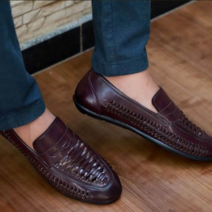 May include: A pair of dark burgundy leather loafers featuring a woven texture across the vamp and sides. The slip-on shoes have a smooth leather toe cap and heel counter, a low profile, and a solid black sole, providing a clean and structured look.