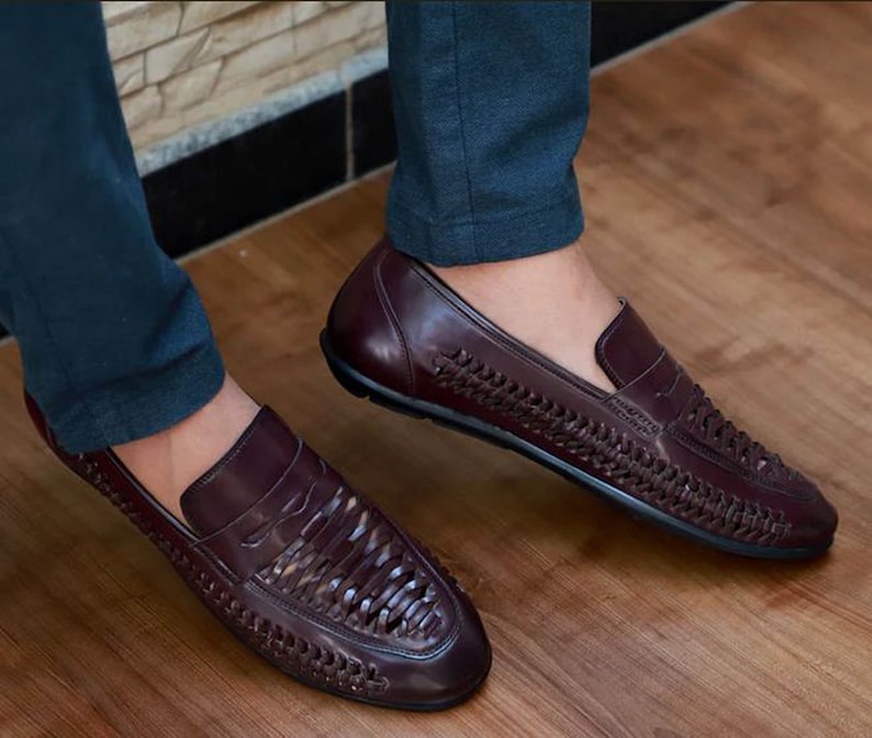 May include: A pair of dark burgundy leather loafers featuring a woven texture across the vamp and sides. The slip-on shoes have a smooth leather toe cap and heel counter, a low profile, and a solid black sole, providing a clean and structured look.