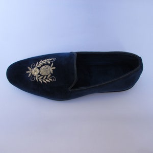 Pode incluir: Um mocassim de veludo azul-marinho com um motivo floral e de abacaxi bordado a fio dourado no peito do p&eacute;. O sapato apresenta uma biqueira arredondada, uma silhueta de perfil baixo e um debrum escuro ao longo da gola, em tecido macio.