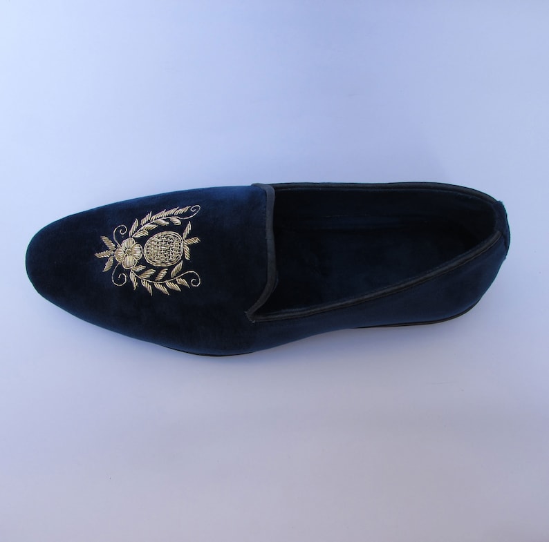 Pode incluir: Um mocassim de veludo azul-marinho com um motivo floral e de abacaxi bordado a fio dourado no peito do p&eacute;. O sapato apresenta uma biqueira arredondada, uma silhueta de perfil baixo e um debrum escuro ao longo da gola, em tecido macio.