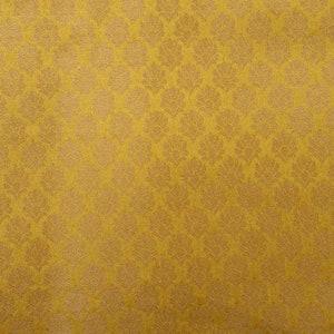 May include: Mustard yellow fabric with a repeating floral pattern. The design features a textured, raised pattern in a lighter shade of gold. The fabric has a subtle sheen, giving it a luxurious appearance. Suitable for upholstery or apparel.