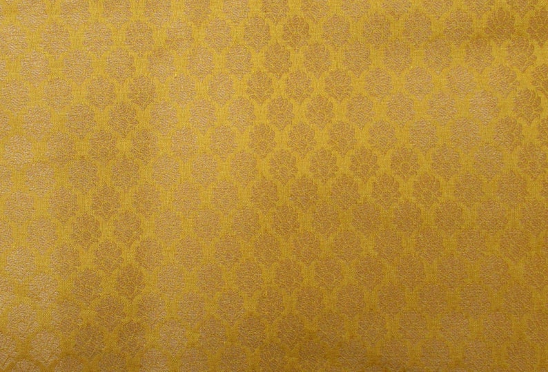 May include: Mustard yellow fabric with a repeating floral pattern. The design features a textured, raised pattern in a lighter shade of gold. The fabric has a subtle sheen, giving it a luxurious appearance. Suitable for upholstery or apparel.