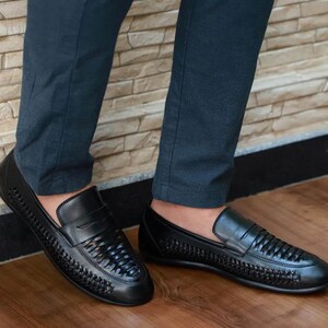 May include: A pair of black leather loafers featuring a woven texture across the vamp and sides. The shoes have a classic penny loafer strap across the top, a rounded toe, and a smooth solid leather heel counter, providing a sleek and uniform look.
