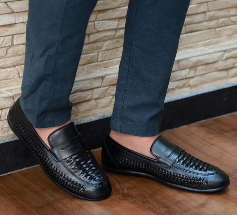 May include: A pair of black leather loafers featuring a woven texture across the vamp and sides. The shoes have a classic penny loafer strap across the top, a rounded toe, and a smooth solid leather heel counter, providing a sleek and uniform look.