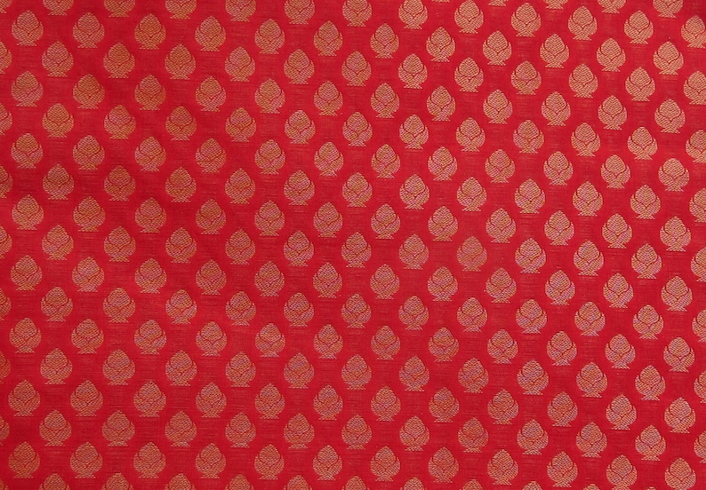 May include: A vibrant red fabric featuring a repeating pattern of small, stylized golden-yellow floral or leaf-like motifs arranged in a structured grid. The design consists of symmetrical, teardrop-shaped elements with intricate internal line details.