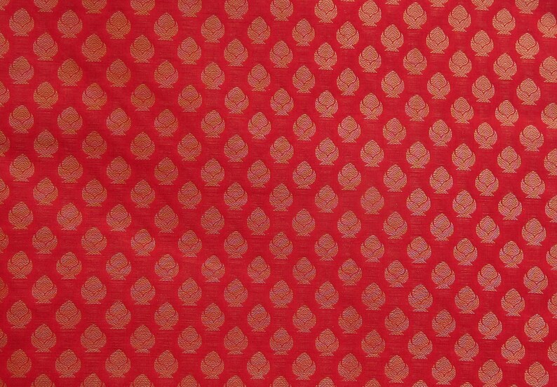 May include: A vibrant red fabric featuring a repeating pattern of small, stylized golden-yellow floral or leaf-like motifs arranged in a structured grid. The design consists of symmetrical, teardrop-shaped elements with intricate internal line details.