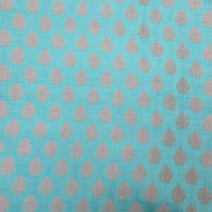 May include: A vibrant turquoise fabric featuring a repeating pattern of small, light-colored, leaf-shaped motifs arranged in a grid. The textile has a visible woven texture, and the light-colored leaf designs are evenly spaced across the surface.