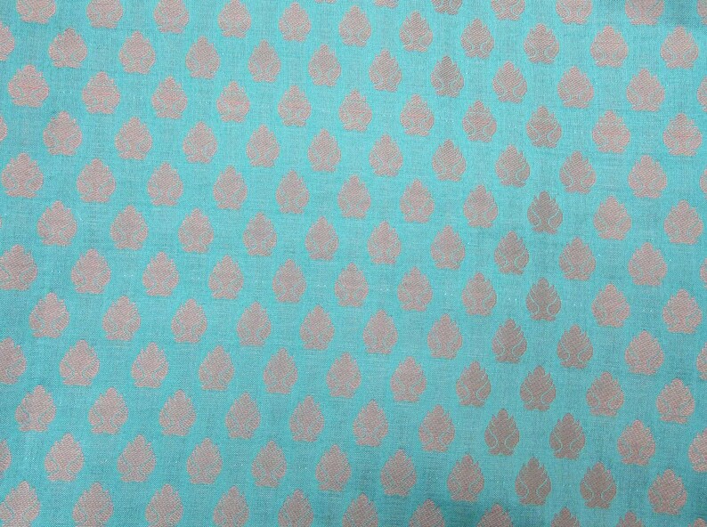 May include: A vibrant turquoise fabric featuring a repeating pattern of small, light-colored, leaf-shaped motifs arranged in a grid. The textile has a visible woven texture, and the light-colored leaf designs are evenly spaced across the surface.