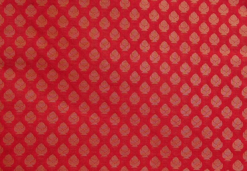 May include: Red fabric with a repeating pattern of stylized, gold-colored floral motifs. The design is evenly spaced across the surface, creating a textured appearance. The fabric has a slight sheen, enhancing the visual appeal.