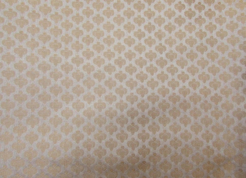 May include: A close-up of a fabric with a repeating pattern of stylized floral shapes in a light beige color. The pattern is set against a lighter, off-white background, creating a subtle contrast and texture.