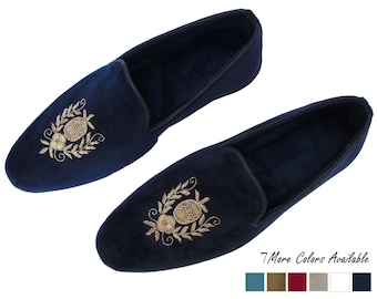 Op de afbeelding: Een paar marineblauwe fluwelen slippers met goudkleurige geborduurde ananas- en bloemmotieven op de wreef. De slippers hebben een donkere rand langs de opening en de tekst 7 More Colors Available met zes kleine gekleurde vierkantjes.