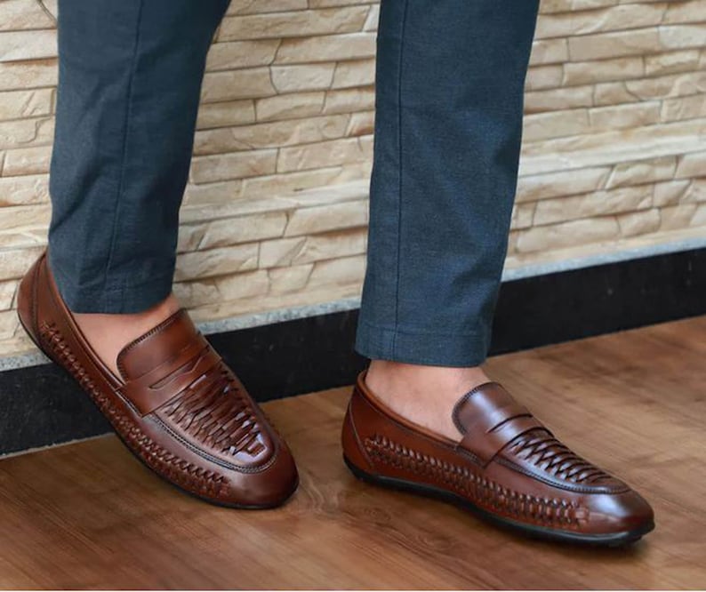 May include: A pair of brown leather loafers featuring a woven texture across the vamp and sides. The shoes have a classic penny loafer strap detail across the top and a smooth, polished finish on the toe and heel sections with a dark sole.