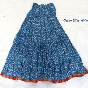 May include: A long, crinkled skirt in an ocean blue color featuring a white floral vine pattern throughout. The skirt has an elasticized waistband and a wide, contrasting dark red border at the hem with a subtle gold-toned dotted detail.