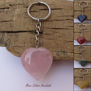 May include: A pink heart-shaped gemstone keyring with a silver ring and chain. The image also shows keyrings in blue, red, green, and yellow. Text at the bottom reads "More Colors Available".