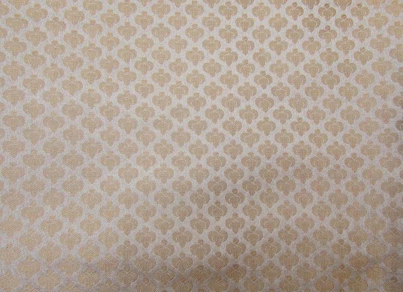 May include: A fabric featuring a repeating pattern of small, light gold spade-like shapes arranged in a grid on a textured, light beige background. The design consists of uniform, symmetrical motifs that create a consistent, dense visual texture.