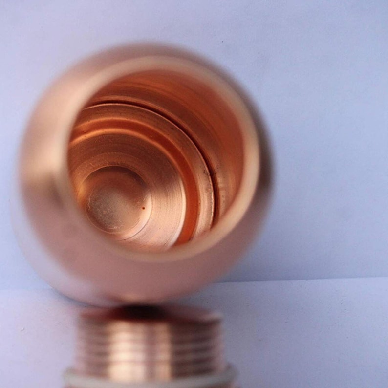 May include: A copper-colored, cylindrical container with a threaded base. The interior of the container is visible, revealing a smooth, reflective surface. The container's opening is round, and the overall design is simple and functional.