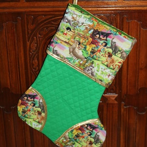 May include: A green quilted Christmas stocking with a gold trim and a colorful print of characters from the Jungle Book.