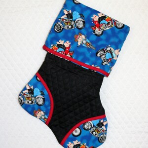 May include: A blue and black Christmas stocking with a quilted black fabric and a blue fabric with a pattern of pigs riding motorcycles. The stocking has a red trim.