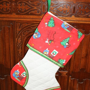 May include: A red and white Christmas stocking with a quilted white section and a red section featuring a Peanuts theme with characters like Snoopy and Woodstock. The stocking has a green and gold trim.