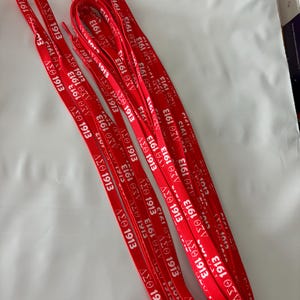 Może przedstawiać: Kilka czerwonych smyczy z białym napisem "ΔΣΘ 1913" ułożonych na białej powierzchni. Smycze są płaskie i mają powtarzający się wzór greckich liter i roku.