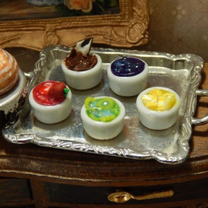 May include: A silver serving tray with five small white bowls filled with different desserts. The bowls contain chocolate, blueberries, strawberries, kiwi, and pineapple.