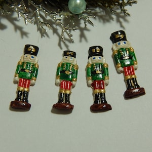May include: Four miniature nutcracker figurines. Each figurine is painted in green, red, black, gold, and white. The nutcrackers are standing on a white surface.