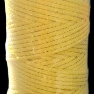 Könnte beinhalten: Eine Spule aus gelbem Baumwollseil, fest gewickelt und in klarem Kunststoff verpackt. Das Seil scheint aus mehreren Strängen zu bestehen, wodurch eine strukturierte Oberfläche entsteht. Die Farbe ist ein helles, sonniges Gelb.
