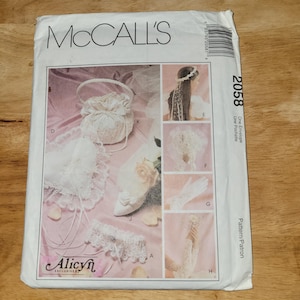 May include: A McCall's 2058 sewing pattern envelope featuring white lace accessories including a drawstring pouch, heart-shaped pillow, garter, headpiece, veil, and gloves. The cover displays the text McCall's 2058 and Alicyn Exclusives.
