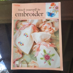 May include: A book titled "Teach Yourself to Embroider" with step-by-step instructions for 15 beautiful designs. The cover features a pink background with embroidered sachets and a butterfly.