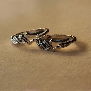 May include: Two silver rings with a unique design. Each ring features a central, stylized arrow shape and a textured band. The rings are marked with "S925". The rings are displayed on a neutral background.