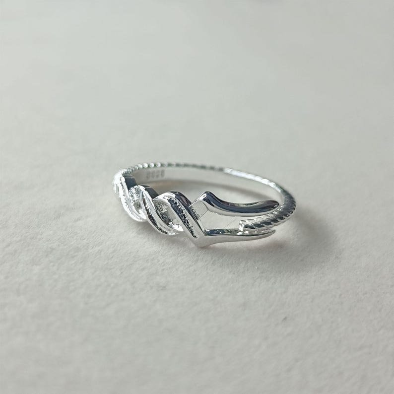 May include: A silver ring with a unique design. The ring features a twisted, rope-like pattern in the center, with a smooth, polished finish. The band has a textured, beaded edge. The ring is shown on a white surface.