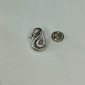 May include: A silver-colored snake lapel pin with intricate detailing, coiled in a stylized design. The pin features a separate backing piece for secure attachment. The snake's head is raised, with a forked tongue visible.