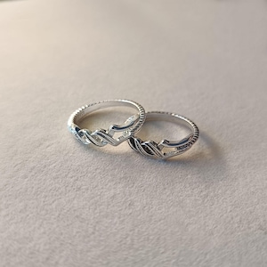 May include: Two silver rings with a braided design. The rings are set against a neutral background, showcasing their intricate details. The rings have a textured band and a woven pattern.
