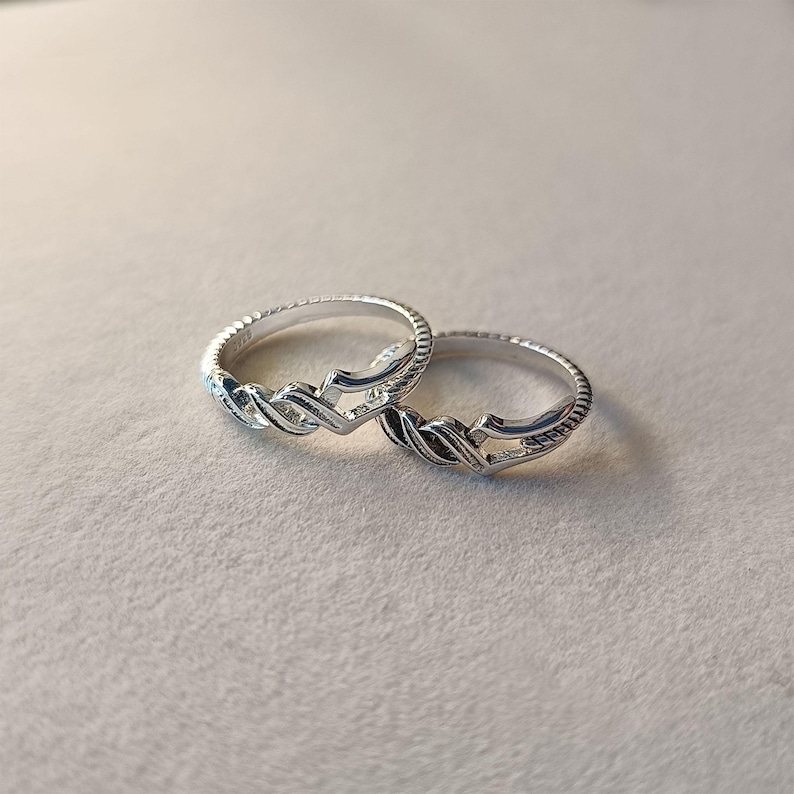May include: Two silver rings with a braided design. The rings are set against a neutral background, showcasing their intricate details. The rings have a textured band and a woven pattern.