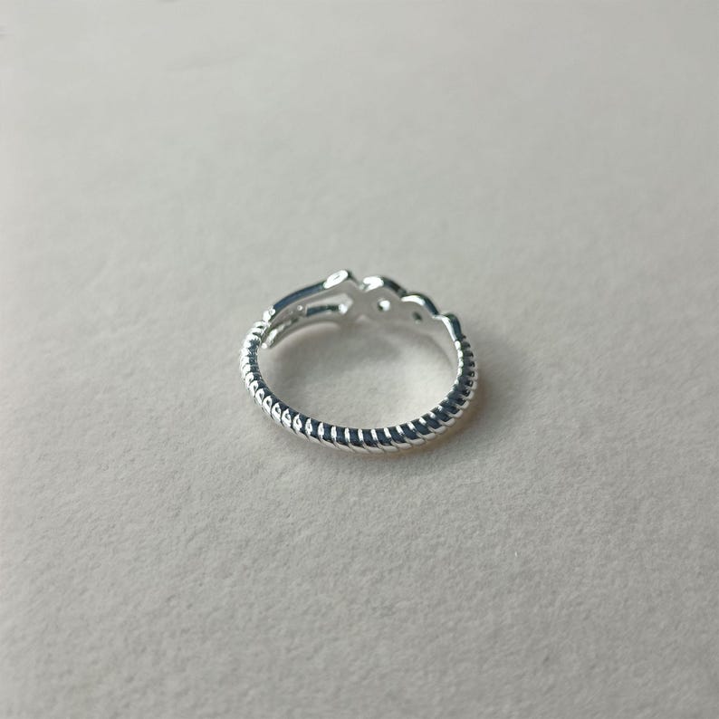 May include: A silver ring with a decorative design. The ring features a textured band and a stylized openwork design on the top. The ring is shown on a neutral background.