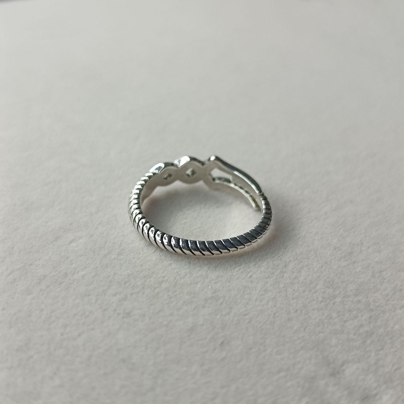 May include: A silver ring with a textured, rope-like band. The ring features three small, diamond-shaped accents at the top. The ring is made of a shiny, metallic material.