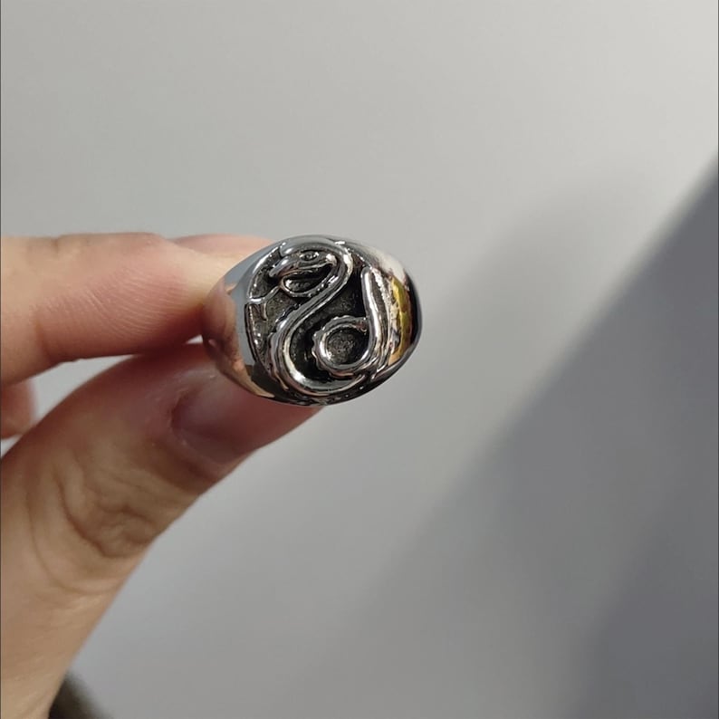 Pode incluir: Um anel prateado com um design detalhado de cobra. A cobra est&aacute; enrolada e centrada na face do anel. O anel tem um acabamento polido e uma forma arredondada.