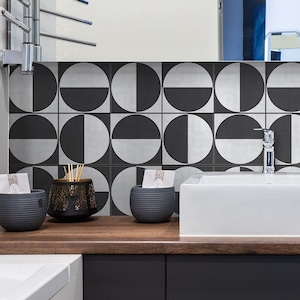 Puede incluir: Un baño moderno con un lavabo de porcelana blanca y armarios negros. El salpicadero es un patrón geométrico de círculos negros y blancos.