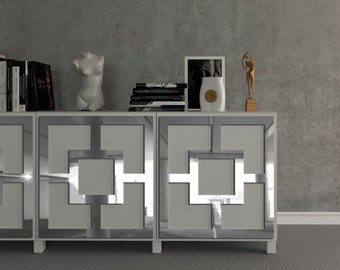 Può includere: Un mobile bianco moderno con disegni geometrici a specchio sulle ante. Il mobile è adornato con oggetti decorativi, tra cui libri, un busto, un vaso, una foto incorniciata e una scultura dorata. Il mobile è posto contro un muro grigio.