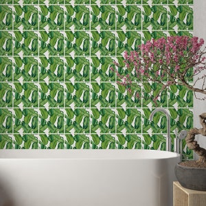 May include: A white bathtub with a green and white tiled wall behind it. A small bonsai tree with pink flowers sits on a wooden stand to the right of the tub.