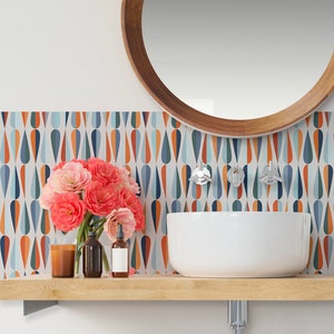 May include: A white bathroom sink with a wooden countertop and a round wooden mirror above it. The wall behind the sink is decorated with a colourful geometric pattern of teardrop shapes in shades of blue, orange, and white.
