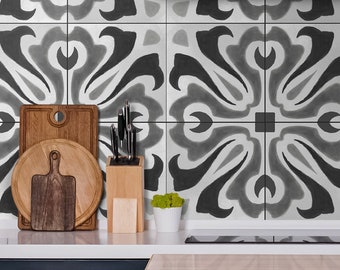 May include: A kitchen backsplash featuring square tiles with a repeating black, gray, and white floral-inspired pattern. The wall is positioned behind a white countertop with a wooden cutting board, a knife block, and a light blue coffee machine.